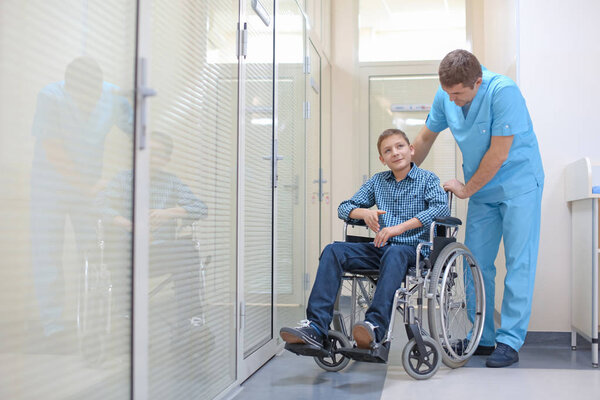 Male doctor taking care of little boy in wheelchair indoors