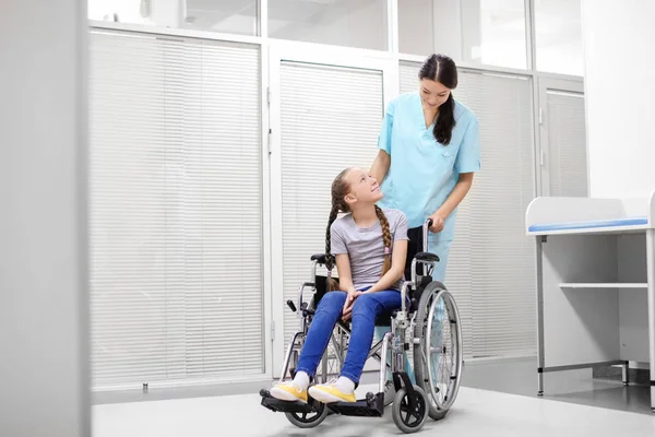 Young female doctor taking care of little girl in wheelchair indoors — Stock Photo, Image