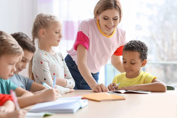 Vrouwelijke leraar kinderen helpen met huiswerk in klas op school — Stockfoto