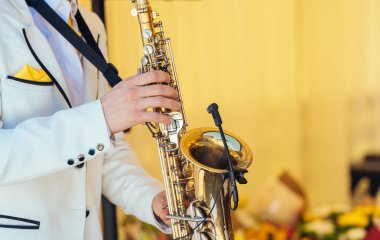 Beyaz ceketli saksafoncu saksafon çalıyor. Düğünde saksafoncu cazcı ve saksafoncu.