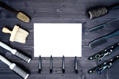Kuaför araçlar ahşap arka plan üzerinde. Kuaför araçlarıyla düz boş kartı yatıyordu. Makas, tarak, fırçaları ve boş beyaz kağıt, boş alan ile toka ile ahşap masa üzerinde üstten görünüm