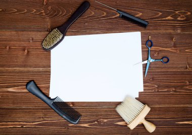 Kuaför araçlar ahşap arka plan üzerinde. Kuaför araçlarıyla düz boş kartı yatıyordu. Makas, tarak ve fırça ile boş beyaz kağıt, boş alan ahşap masa üzerinde üstten görünüm