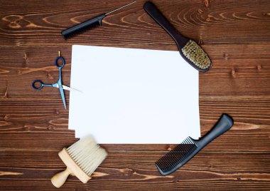 Kuaför araçlar ahşap arka plan üzerinde. Kuaför araçlarıyla düz boş kartı yatıyordu. Makas, tarak ve fırça ile boş beyaz kağıt, boş alan ahşap masa üzerinde üstten görünüm