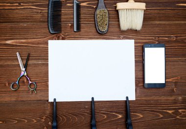 Kuaför araçlar ahşap arka plan üzerinde. Kuaför araçlarıyla düz boş kartı yatıyordu. Ahşap masa görünümü makasla top, tarak ve fırça boş beyaz kağıt ve telefon, kopya alanı ile