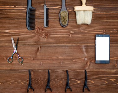 Kuaför araçlar ahşap arka plan üzerinde. Üstten görünüm makas, tarak, fırça ve toka ile telefon, boş alan ahşap tablo