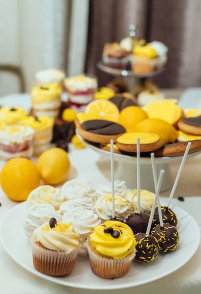 Cake pops, marshmallows and cupcakes on wedding candy bar, selective focus. Holiday candy bar in yellow and brown color