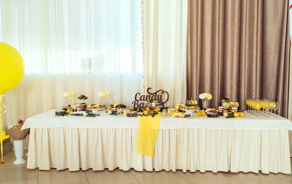 Holiday candy bar in yellow and brown color. Wedding candy bar served with cupcakes, cake pops, desserts in glasses, lemons and coffee beans