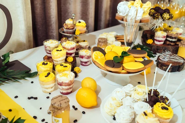 Holiday candy bar in yellow and brown color. Wedding candy bar served with lemon biscuits, cake pops, desserts in glasses, lemons and coffee beans