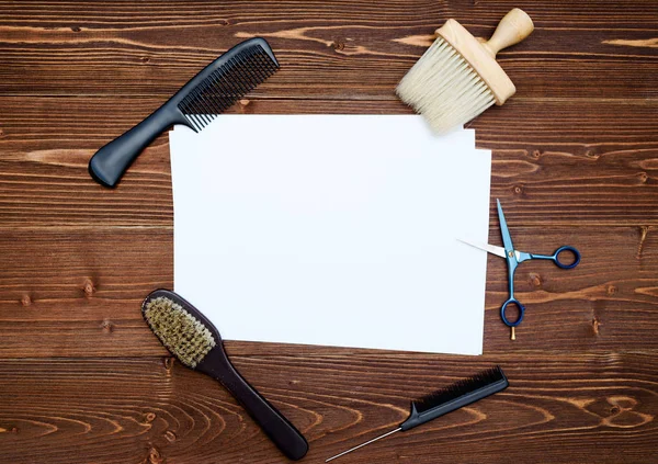 Kuaför araçlar ahşap arka plan üzerinde. Kuaför araçlarıyla düz boş kartı yatıyordu. Makas, tarak ve fırça ile boş beyaz kağıt, boş alan ahşap masa üzerinde üstten görünüm