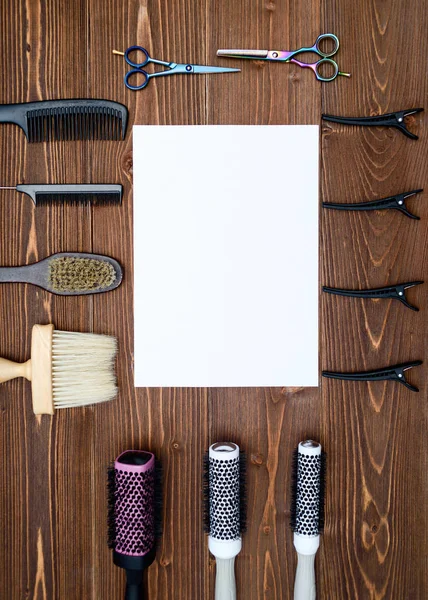 Kuaför araçlar ahşap arka plan üzerinde. Kuaför araçlarıyla düz boş kartı yatıyordu. Makas, tarak, fırçaları ve boş beyaz kağıt, boş alan ile toka ile ahşap masa üzerinde üstten görünüm