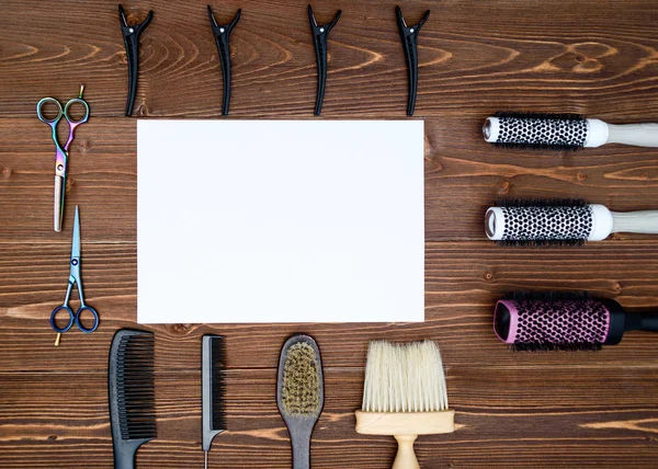 Kuaför araçlar ahşap arka plan üzerinde. Kuaför araçlarıyla düz boş kartı yatıyordu. Makas, tarak, fırçaları ve boş beyaz kağıt, boş alan ile toka ile ahşap masa üzerinde üstten görünüm