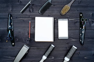 Kuaför araçlar ahşap arka plan üzerinde. Kuaför araçlarıyla düz boş kartı yatıyordu. Üstten görünüm makas, tarak ve toka ile boş defter, kalem ve telefon, boş alan ahşap tablo