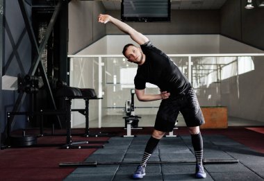 Genç adam eğitim önce kasları hazırlanıyor. Spor salonunda egzersiz kas atlet. Germe adam uygun. Isınma-up profesyonel sporcu. Tam vücut uzunluğu portre