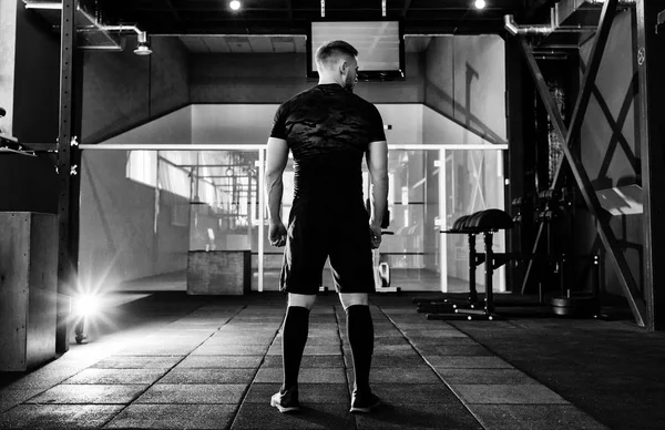 Young man preparing muscles before training, back view . Muscular athlete exercising crossfit. Workout lifestyle concept.  Full body length portrait