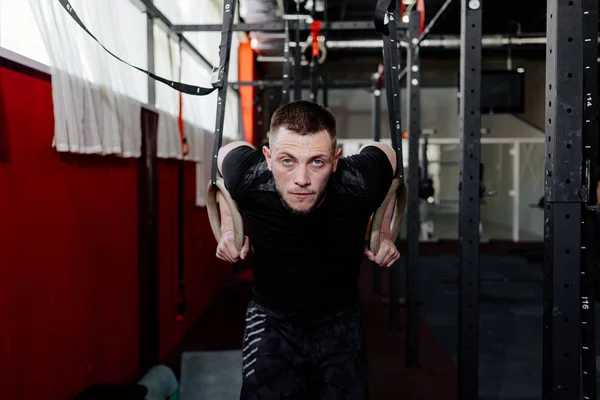 Athlete working out his muscles on rings. Man working out in gym pull ups with gymnastic rings