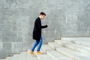 Ekose gömlek ve merdivenlerden yukarı yürümek ve açık havada smartphone kullanarak kot şık genç adam. Üst katta, boş alan yürüyüş smartphone ile öğrenci