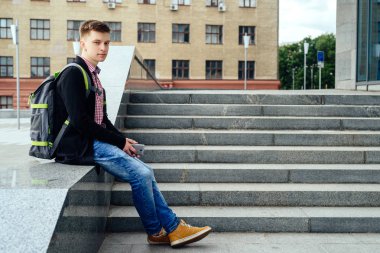 Yakışıklı delikanlı taş merdiven yanında oturan ve akıllı telefon şehir mekanlarda kullanma sırt çantası ile. Üniversiteden sonra tam vücut öğrenci aittir