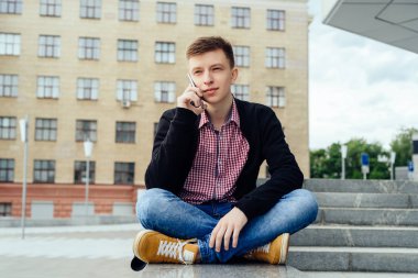 Taş merdiven yanında oturan ve akıllı telefon şehir havada konuşurken mutlu yakışıklı genç adam. Öğrenci üniversite açık havada sonra aittir