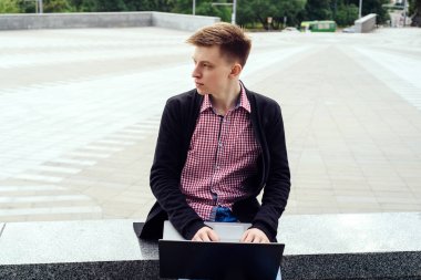 Ceket ve oturma ve açık havada dizüstü bilgisayarda yazarak kot şık genç adam. Teknoloji ve iletişim kavramı 