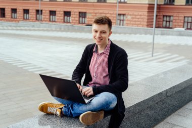 Ceket ve oturma ve açık havada dizüstü bilgisayarda yazarak kot şık genç adam. Teknoloji ve iletişim kavramı 