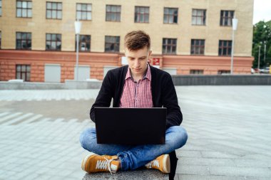 Ceket ve oturma ve açık havada dizüstü bilgisayarda yazarak kot şık genç adam. Teknoloji ve iletişim kavramı 