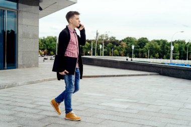 Ekose gömlek ve kot el şehirde yürüyüş ve tam vücut açık havada, cep telefonuyla konuşurken dizüstü bilgisayar ile şık genç adam. Öğrenci ile hareket eden telefon