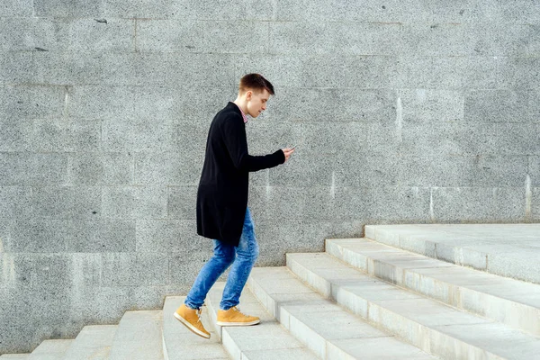 Ekose gömlek ve merdivenlerden yukarı yürümek ve açık havada smartphone kullanarak kot şık genç adam. Üst katta, boş alan yürüyüş smartphone ile öğrenci