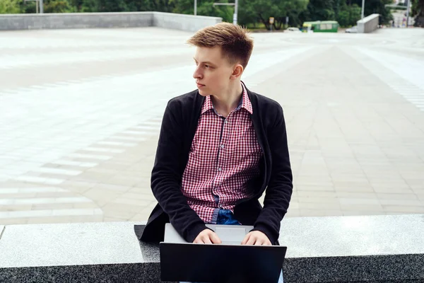 Ceket ve oturma ve açık havada dizüstü bilgisayarda yazarak kot şık genç adam. Teknoloji ve iletişim kavramı 