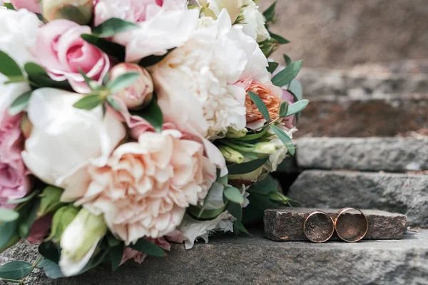 İki altın alyans beyaz ve pembe şakayık ve gül güzel düğün buket yakınındaki taş kadar açık havada, yakın görüntü