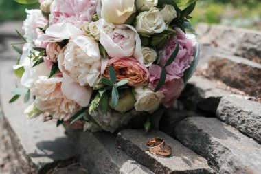 İki altın alyans beyaz ve pembe şakayık ve açık havada, gül güzel düğün buket yakınındaki taş yakın çekim