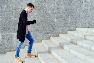 Ekose gömlek ve merdivenlerden yukarı yürümek ve açık havada smartphone kullanarak kot şık genç adam. Üst katta, boş alan yürüyüş smartphone ile öğrenci