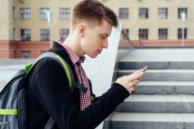Şehirde yürüyüş ve açık havada smartphone kullanarak sırt çantası ile ekose gömlekli şık genç adam. Öğrenci ile yürüyüş smartphone 