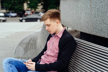 Şehirde bankta oturmuş akıllı telefon kullanan rahat genç adam. Holding ve seyir mobil akıllı telefon açık havada ceketli yakışıklı öğrenci