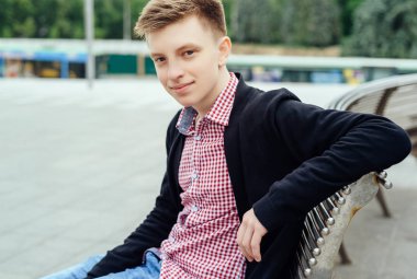 Ekose gömlek ve ceket şehir havada bankta oturmuş rahat genç adam portresi. Öğrenci seyahat