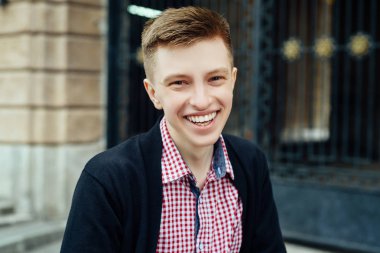 Genç yakışıklı trendy gülümseyen adam şehirde, ekose gömlekli portresi bulanıklık açık havada kameraya bakıyor