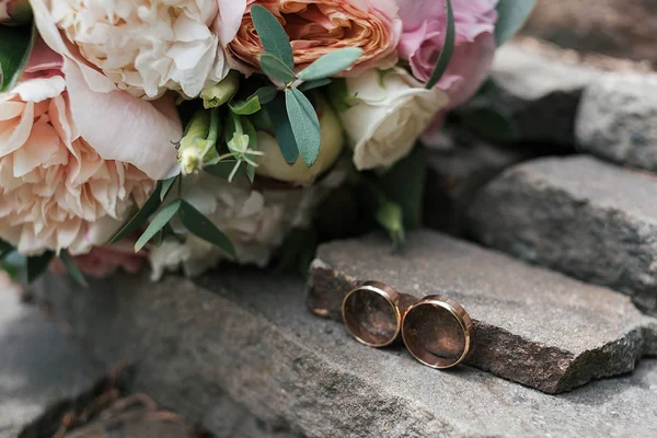 İki altın alyans beyaz ve pembe şakayık ve gül güzel düğün buket yakınındaki taş açık havada, seçici odak bulanıklık, yakın çekim