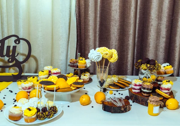Holiday candy bar in yellow and brown color. Wedding candy bar served with cupcakes, cake pops, biscuits, desserts in glasses, lemons and coffee beans