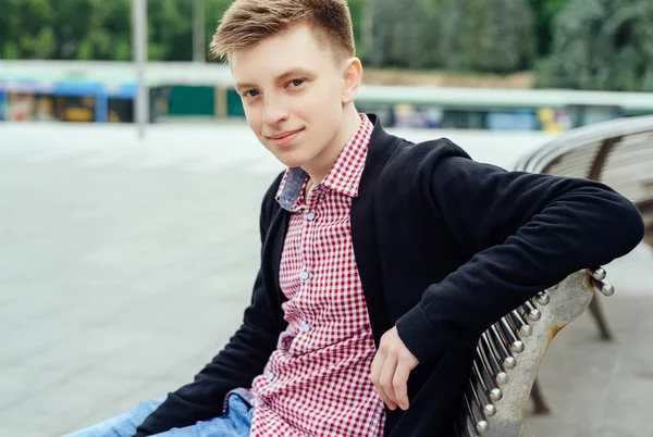 Ekose gömlek ve ceket şehir havada bankta oturmuş rahat genç adam portresi. Öğrenci seyahat