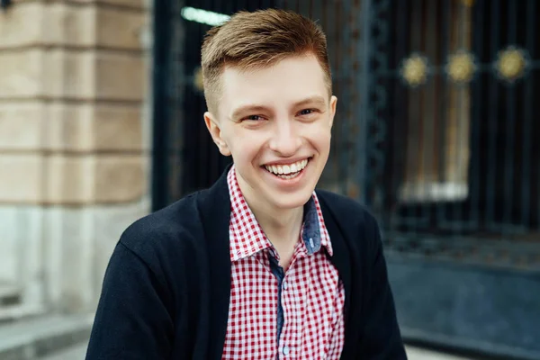 Genç yakışıklı trendy gülümseyen adam şehirde, ekose gömlekli portresi bulanıklık açık havada kameraya bakıyor