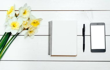 Nergis Beyaz ahşap zemin üzerine sarı buket. Boş kart düz yatıyordu. Nergis, boş günlüğü, kalem ve telefon, boş alan, beyaz ekran ile tabloda üstten görünüm
