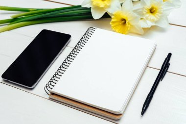 Nergis Beyaz ahşap zemin üzerine sarı buket. Boş kart düz yatıyordu. Nergis, boş günlüğü, kalem ve telefon, boş alan tablo üstten görünüm