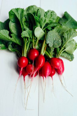 Taze organik kırmızı radishe üstleri ve beyaz ahşap zemin üzerine yeşil yaprakları ile demet. Sebze arka plan