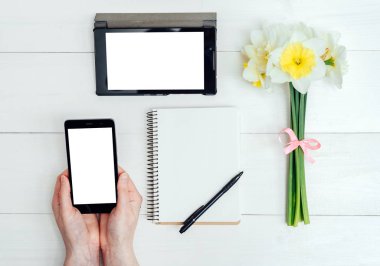 Üstten görünüm nergis, boş günlüğü, tablet ve cep telefonu ile beyaz perde, boş alan ile kızın el ile masada. Kızın ellerini günlüğüne yazma