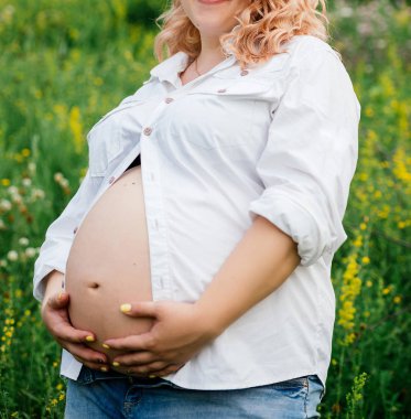 Genç hamile kadının karnı elleriyle dokunuyor. Hamile kadının karnında kırpılmış görüntü. Hamile kadının karnı sarılma