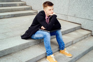 Üzgün dalgın genç adam ceket ve kot ile dizüstü bilgisayar açık havada, merdivenlerde oturan çene üzerinde el ile boş alan. Teknoloji ve iletişim kavramı 