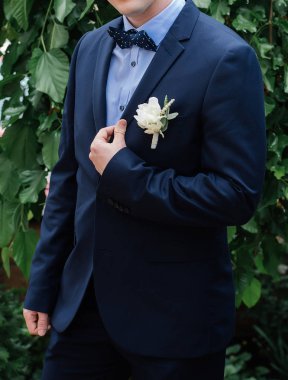 Şık damat açık havada mavi takım elbise, papyon ve yaka çiçeği. Damat yaka ceketinin holding