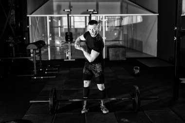 Genç adam onun pazı spor salonunda gösterilen siyah t-shirt giymiş çığlık. Spor salonunda poz ve onun pazı gösterilen süre kameraya bakarak adam