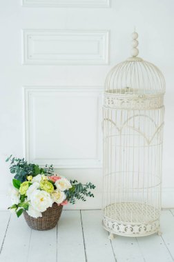 Beyaz vintage dekoratif kuş kafes ve güzel çiçek aranjmanı sepette önünde beyaz duvar, boş alanı