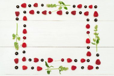 Beyaz ahşap zemin, boş alan üzerine üstten görünüm çerçevesinin tatlı taze organik ahududu, böğürtlen kiraz ve yeşil yapraklar ve çiçekler. Yaz ve sağlıklı gıda kavramı 