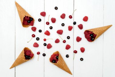 Üstten görünüm tatlı taze organik ahududu ve gözleme koniler ve meyveler siyah kuş üzümü, boş alan. Taze çilek Beyaz ahşap arka plan boşluk. Yaz ve sağlıklı gıda kavramı